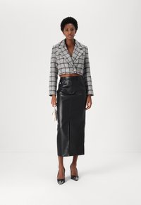 Kuttet tweed-blazer i svart og hvitt med brede revers, paret med et svart lær midi-skjørt. Modellen holder en liten hvit håndveske.
