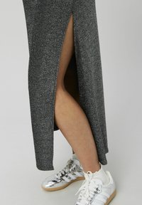 Robe maxi métallisée grise avec une fente haute sur le côté, associée à des baskets blanches et argentées avec des accents rayés et des semelles texturées.