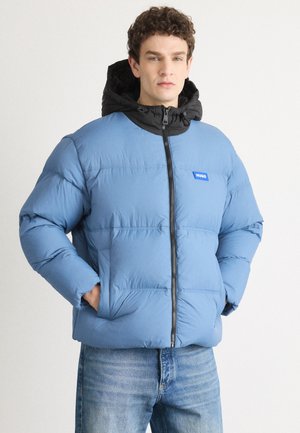 Blue insulated puffer jacket with a black hood, front zipper, and logo patch. Features quilted design, side pockets, and a relaxed fit.