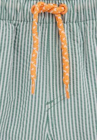 Zeleno in belo črtasta tkanina z oranžnim in belim pletenim vrvico, vpeto skozi oranžne okrogle luknje.