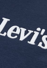 Σκούρο μπλε ύφασμα με λευκό κεντημένο λογότυπο "Levi's", με απαλή υφή και καθαρά, έντονα γράμματα.