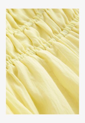 Světle žlutá tkanina se shromážděnou texturou, s elastickými švy pro řasený vzhled. Měkký a lehký materiál.