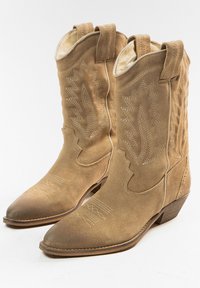 Botas de vaquero de ante en color marrón claro con punta afilada, costuras decorativas y tiradores. El tacón es bajo y la textura es suave.