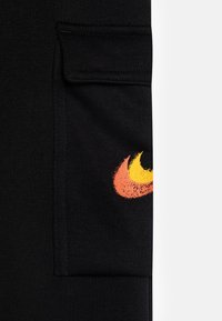 Black athletic pants with a side pocket and a textured flame graphic in red, orange, and yellow on the lower leg. Soft fabric.