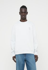 Ανοιχτό γκρι φούτερ από βαμβακερό μείγμα με ριμπ μανσέτες και τελείωμα. Διακοσμημένο με μικρά μαύρα λογότυπα μάρκας στο στήθος. Φοριέται με μπλε τζιν.