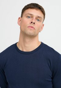 Mørkeblå genser med rund hals, ribbet krage og glatt, teksturert stoff. Har lange ermer og en tettsittende silhuett.