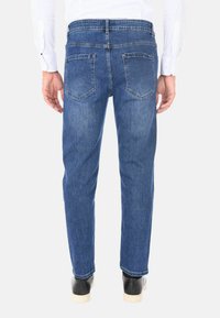 Jeans in denim blu con vestibilità dritta, design a cinque tasche e cuciture visibili. Indossati con una camicia bianca a maniche lunghe e scarpe nere.