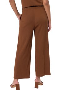 Pantalon marron à jambes larges en tissu texturé, avec une taille haute et des poches latérales. Le design est simple avec une finition lisse.