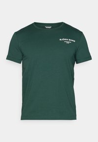 Mørkegrønn bomull t-skjorte med rund hals, korte ermer og hvittrykket logo "BJÖRN BORG STOCKHOLM 1986" på øvre venstre side.