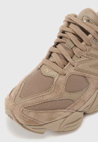 Chaussure de sport en suède beige et mesh, dotée de superpositions texturées, d'une languette rembourrée et de lacets ronds. Logo 'N' discret sur le côté latéral.