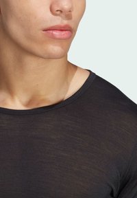Czarna dopasowana koszulka z okrągłym dekoltem, wykonana z lekkiego materiału. Posiada gładką teksturę i subtelną poświatę. Zbliżenie na szyję modela.