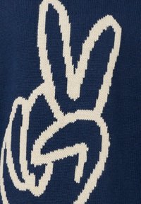 Granatowy sweter z dużym, białym, plecionym wzorem znaku pokoju. Tekstura jest miękka, z widocznymi prążkowaniami i detalami szwów.