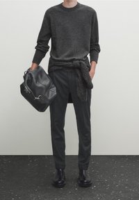 Un pull en laine gris foncé associé à un pantalon charbon et des bottes en cuir noires. Un sac à dos en cuir noir est porté, avec un châle tricoté noué autour de la taille.