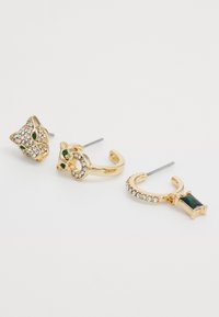 Trois paires de boucles d'oreilles en or : un design de chat avec des accents verts et des strass, un anneau orné de strass, et une pierre précieuse rectangulaire verte.