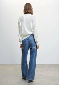 Biały sweter z dzianiny o luźnym kroju, zestawiony z dżinsami o wysokim stanie i szerokich nogawkach w kolorze niebieskim. Prosty design, casualowy styl i miękka faktura.