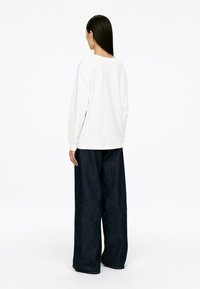 White long-sleeve top paired with dark blue wide-leg jeans. The top features a round neckline, while the jeans have a classic denim texture.