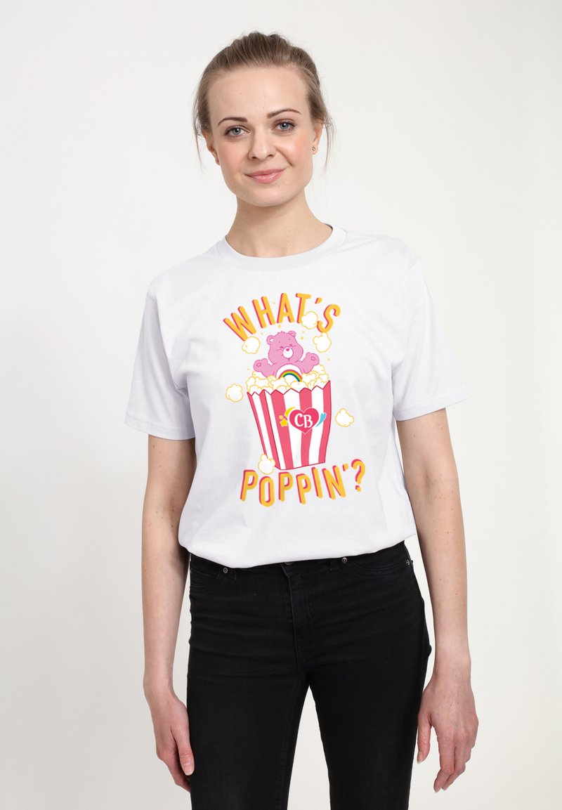 Hvid bomulds T-shirt med et farverigt grafisk design af en lyserød bjørn, der springer ud af en stribet popcornskuffe med teksten "HVAD SKEJER?"
