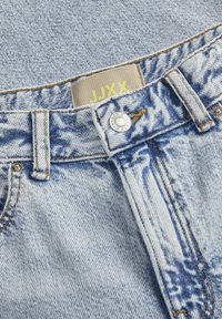 Jeans in denim blu chiaro con una trama prominente, caratterizzati da cuciture dorate, una chiusura con bottone argentato e un'etichetta beige con la scritta "JJXX".