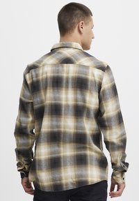 Langermet, rutete skjorte i beige, svart og blå. Har en avslappet passform, knapper ved ermene, og en buet kant. Synlig bomullsstoff.