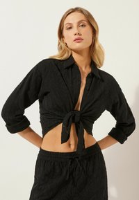 Camicia nera a maniche lunghe con una trama strutturata e nodo sul davanti. Abbinata a pantaloni corti neri con cordoncino coordinato.