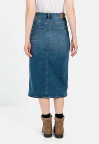 Denim midi nederdel, mørkeblå, med lige snit, to baglommer og en kant, der lige går under knæet. Båret med brune ankelstøvler.