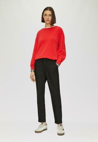 Rode sweatshirt met wit en zwart gestreepte manchetten, gecombineerd met zwarte broeken en lichte sneakers met accenten. Glad materiaal en een ontspannen pasvorm.