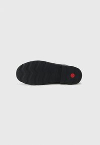 Black rubber shoe sole with textured zigzag pattern and a red circular accent. Features a smooth, flat base for grip and stability.