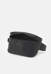 Schwarzlederne Gürteltasche mit glatter Textur, geschwungener Form, Reißverschluss und geprägt Logo auf der Vorderseite. Das Innere ist ungefüttert.