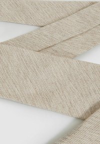 Vävt textilband i ljus beige med ett subtilt fiskbensmönster. Mjuk textur, platt design och klippt i en lång, smal form.