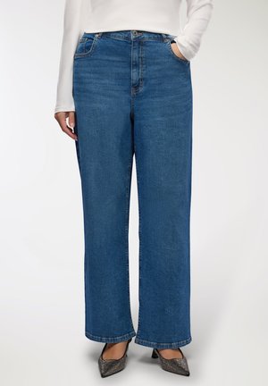 Jeans in denim blu a gamba larga con vita alta, dotati di tasche frontali e orlo rifinito. Indossati con tacchi a punta.
