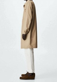 Cappotto beige fino al ginocchio con colletto, abbinato a pantaloni bianchi dritti e scarpe in suede marrone. Tessuto morbido con un design minimalista.
