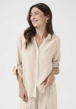 Chemise boutonnée beige clair en tissu doux avec un col rond et des manches retroussées. Se caractérise par une coupe décontractée et un design minimaliste.