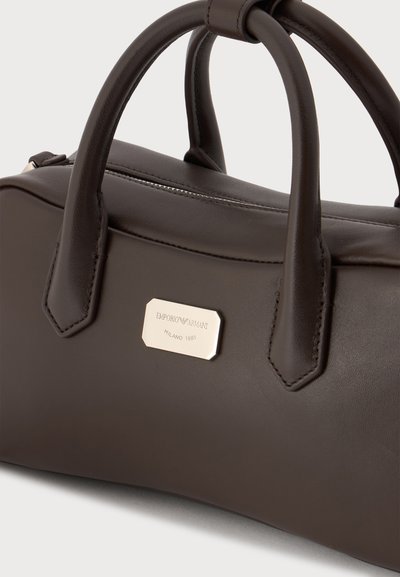 Sac à main en cuir marron foncé avec deux poignées arrondies et une plaque métallique avec le logo Emporio Armani Milano 1981 à l’avant.