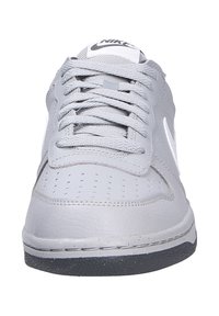 Sneaker in pelle grigia con punta perforata, linguetta in tessuto, lacci piatti e accenti bianchi del logo Nike Swoosh. Suola in gomma nera.