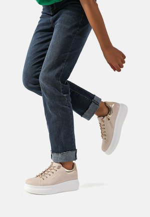 Sneakers rosa chiaro con dettagli metallici, punta rotonda, suola piatta e design con lacci, abbinate a jeans scuri con risvolto.