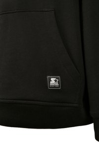 Poche de sweat à capuche noire avec un petit patch rectangulaire du logo Starter Black Label cousu près du bord inférieur.