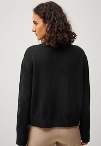 Schwarzer Strickpullover mit strukturierter Oberfläche, lockerer Passform, überschnittenen Schultern und gerippten Bündchen sowie Saum. Rückansicht gezeigt.