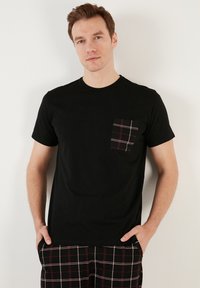 Fekete, rövid ujjú póló, 100% pamutból készült, fekete, fehér és piros kockás zsebbal. Az illeszkedése laza.