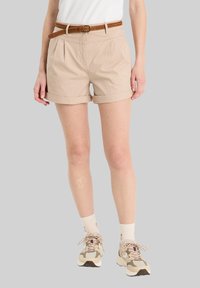 Beige Baumwollshorts mit umgekrempelten Säumen, gefaltenem Vorderteil und einem geflochtenen braunen Gürtel. Tragen mit crèmefarbigen Socken und hellbeigen Sneakers.