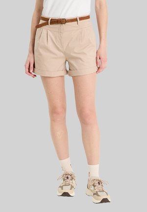 Beige bomuldsshorts med oprevet kant, folder foran og et flettet brunt bælte. Båret med kremfarvede sokker og lyse beige sneakers.