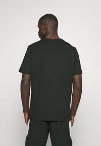 Svart bomullströja med korta ärmar, rundad halsringning och avslappnad passform. Hjälplig yta, bakvy. T-shirten bärs med svarta byxor.