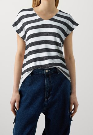 Frau trägt ein schwarz-weiß gestreiftes Kurzarmoberteil mit V-Ausschnitt und dunkelblaue, hochtaillierte Jeans.