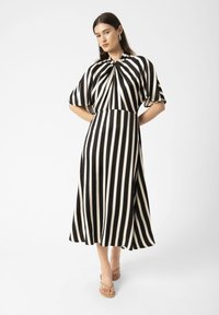 Black and white striped dress with short sleeves, gathered neck detail, A-line silhouette, and smooth fabric. Worn with tan sandals.