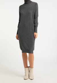 Abito a collo alto grigio in maglia con maniche lunghe, spacchi laterali e polsini a coste. Abbinato a stivali alla caviglia beige. Texture morbida.