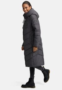 Long, gray puffer coat with a hood, diagonal quilted panels, front zip closure, and side pockets, paired with black lace-up boots.