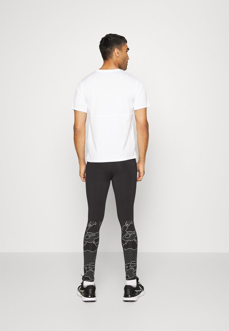 Weißes, kurzes, ärmelloses Sportshirt; figurbetonte schwarze Leggings mit abstrakten weißen Grafiken und strukturierten Akzenten; getragen mit schwarzen Sportschuhen.