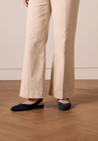 Décolleté in camoscio blu navy con punta affusolata, indossate con pantaloni palazzo beige chiaro, esposte su un pavimento in legno.