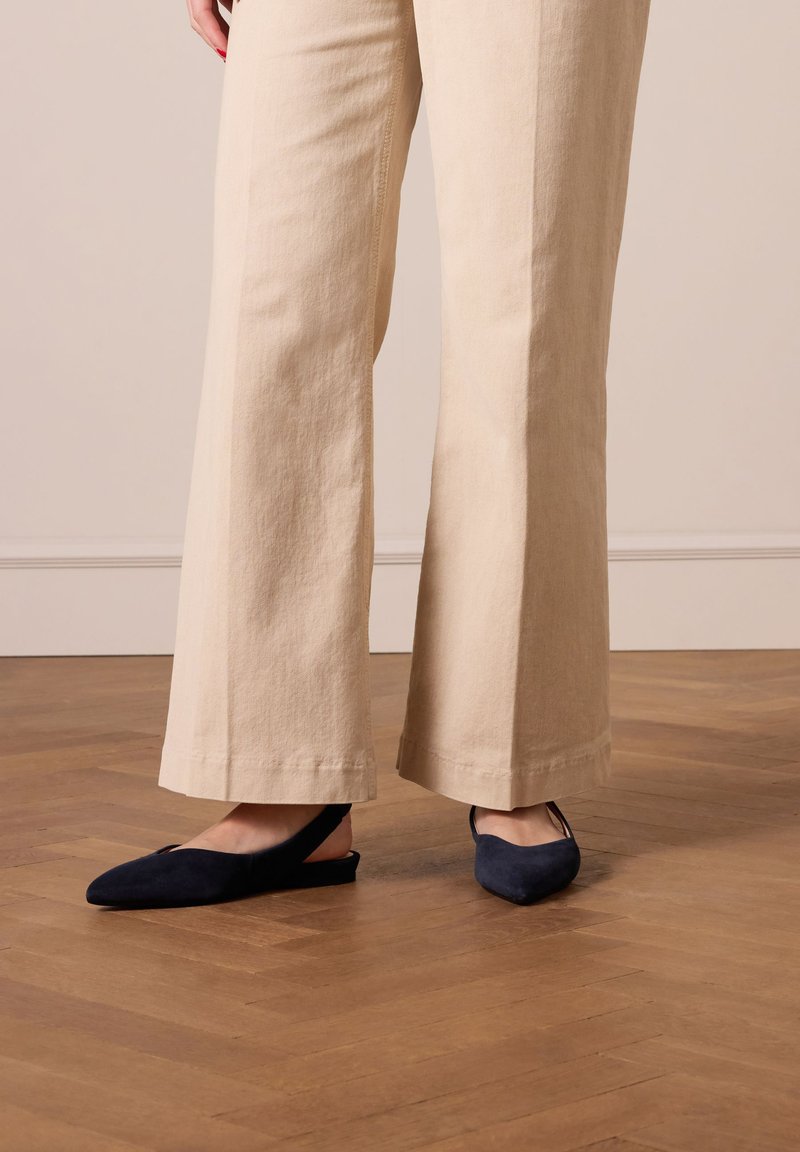 Décolleté in camoscio blu navy con punta affusolata, indossate con pantaloni palazzo beige chiaro, esposte su un pavimento in legno.