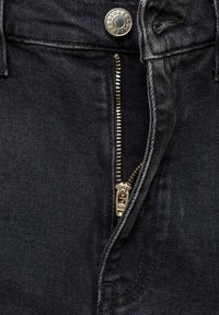 Černé džíny z denimu mají zip na přední straně se zlatým zipem a stříbrným knoflíkem v pase. Viditelná je texturovaná tkanina.