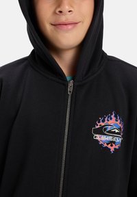 Sweatshirt preto com fecho éclair e um logótipo frontal com chamas em laranja, azul e preto. Confeccionado em tecido macio com um capuz estruturado.